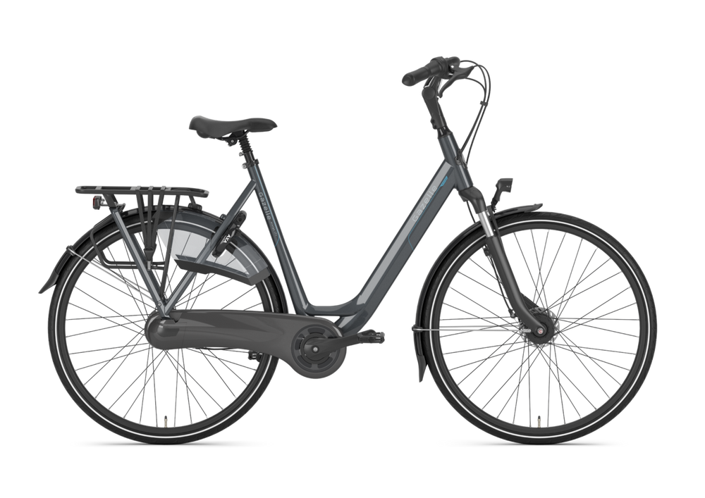 Billede af Gazelle Orange C7+ damecykel i anthracite grey, der står på en grusvej med grønne træer i baggrunden. Cyklen har en klassisk ramme, komfortable saddel og skærme.