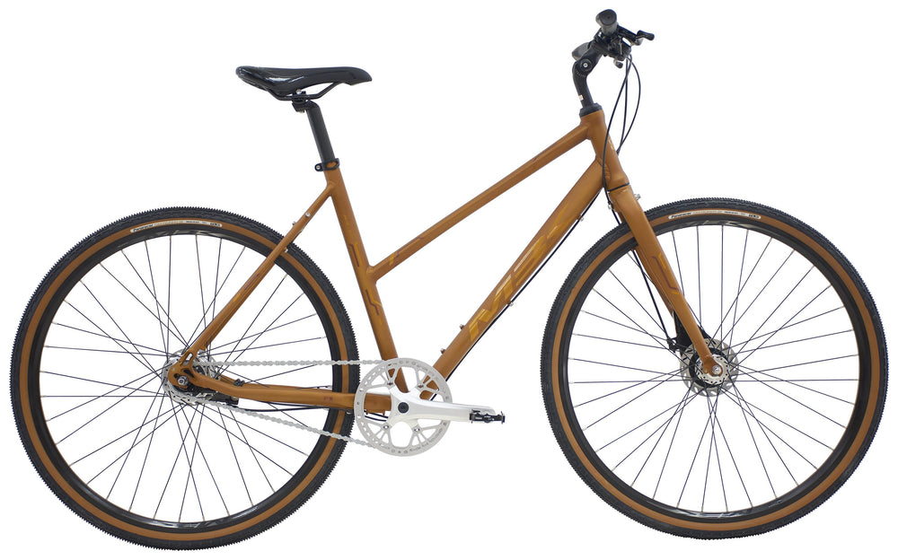 Cykel i kobberfarve med sorte dæk og stel, MBK Octane Gravel Urban Dame, står på en grusvej.