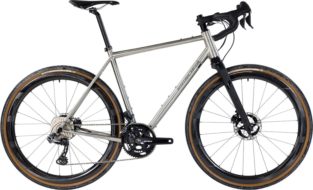 Cykel i titanium med SRAM Rival AXS, Principia Gravel 22, på grusvej med natur i baggrunden.