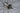 Hvid keramik vase med en moderne, minimalistisk design, placeret på en lys overflade med grønne planter i baggrunden.
